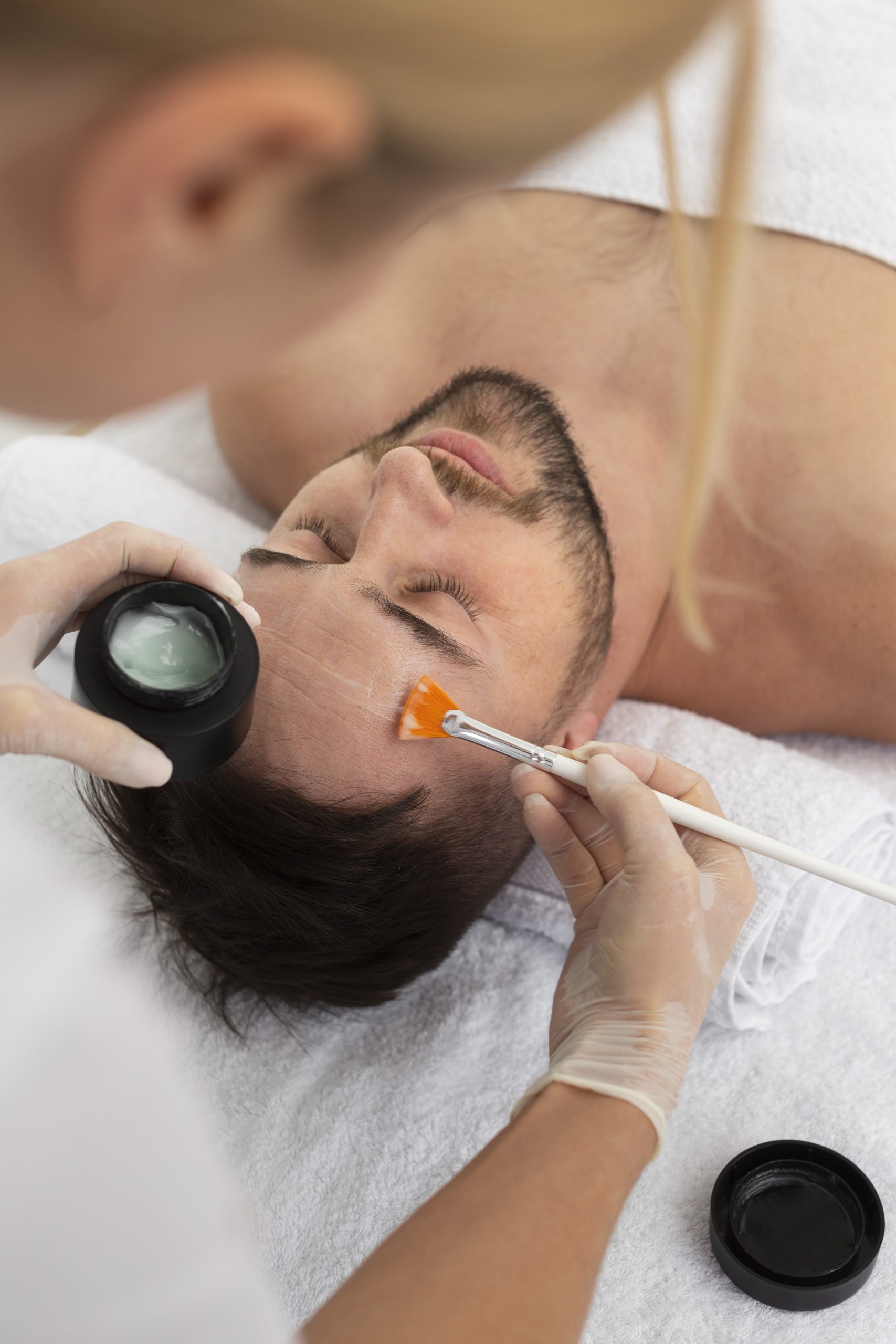 Aplicación de tratamiento facial a hombre tumbado